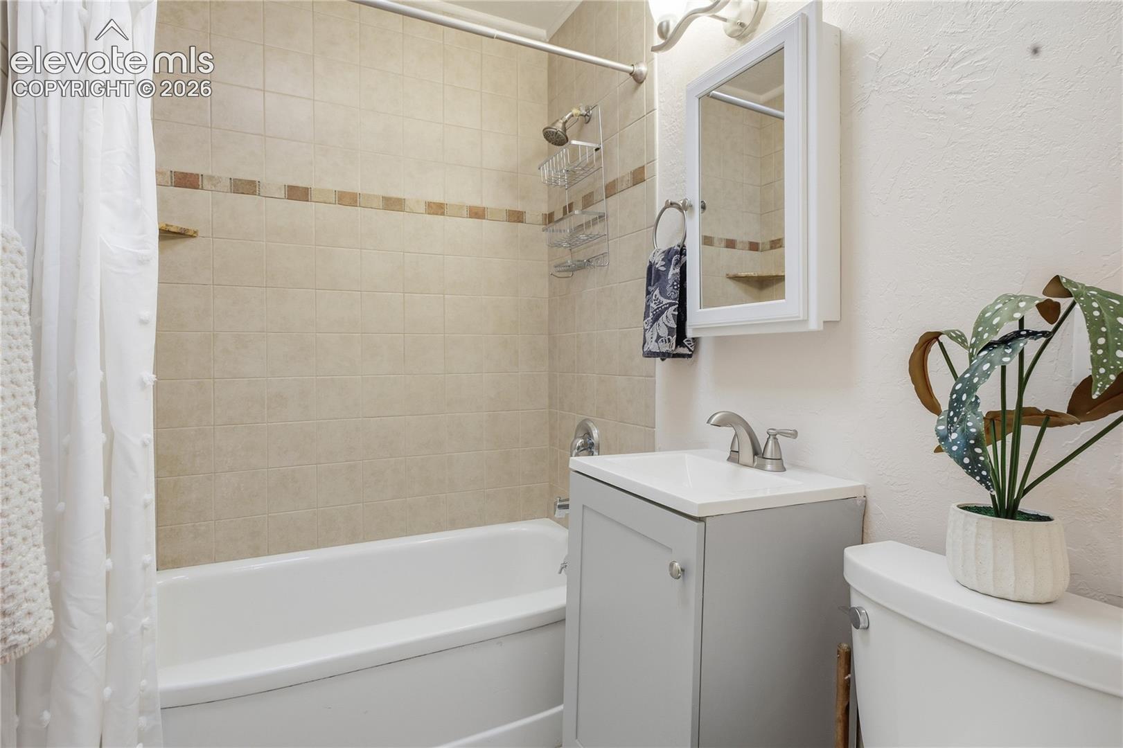 Bathroom featuring a neutral tile shower surround with an inlaid decorative border, a white bathtub, a grey vanity with a rectangular sink, and a wall-mounted mirrored medicine cabinet