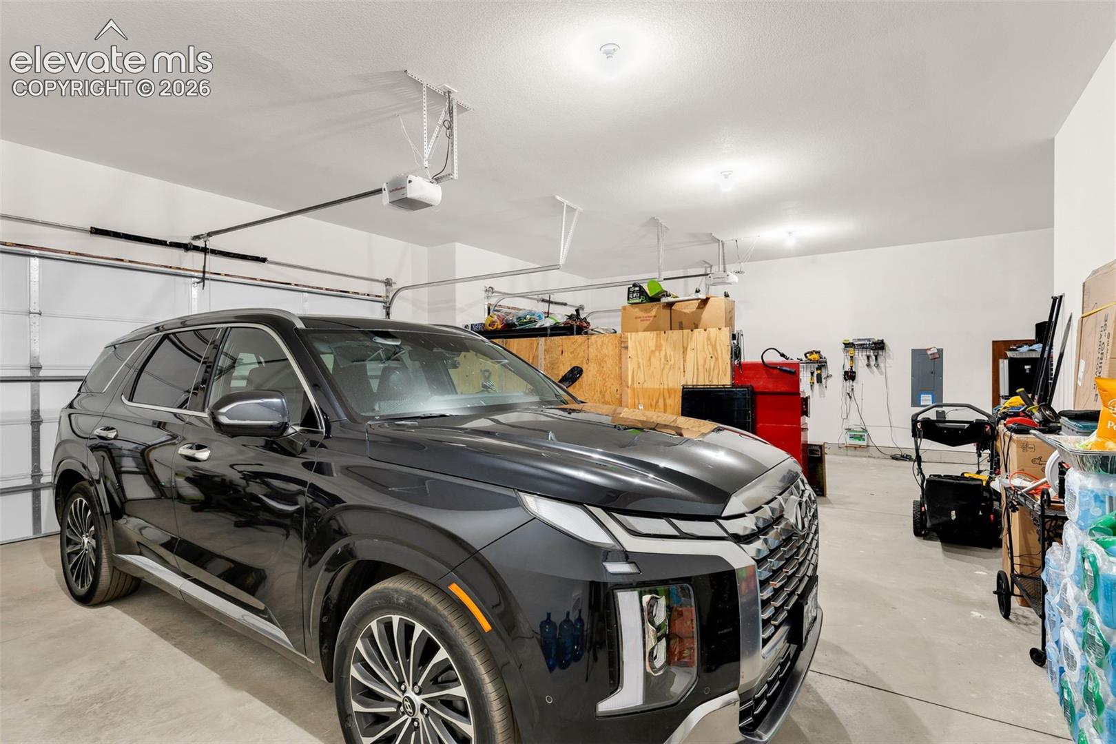 Spacious garage featuring a concrete floor, white walls, multiple overhead lighting fixtures, and an automatic garage door opener