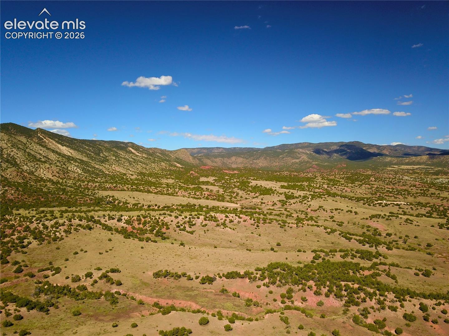 Expansive landscape featuring distant mountains, rolling terrain, and scattered vegetation under a clear sky