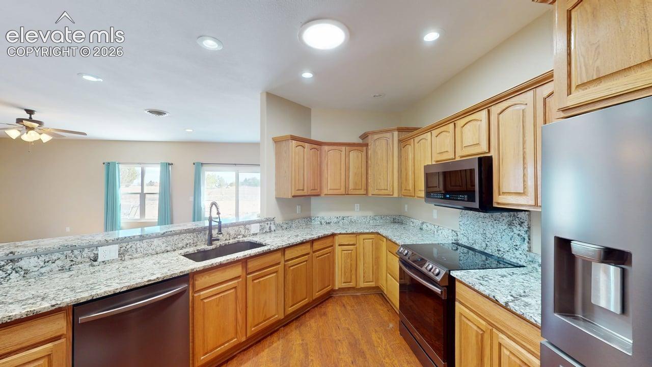 Kitchen featuring granite countertops, wood-finish flooring, wood cabinetry, built-in microwave, and a stainless steel refrigerator