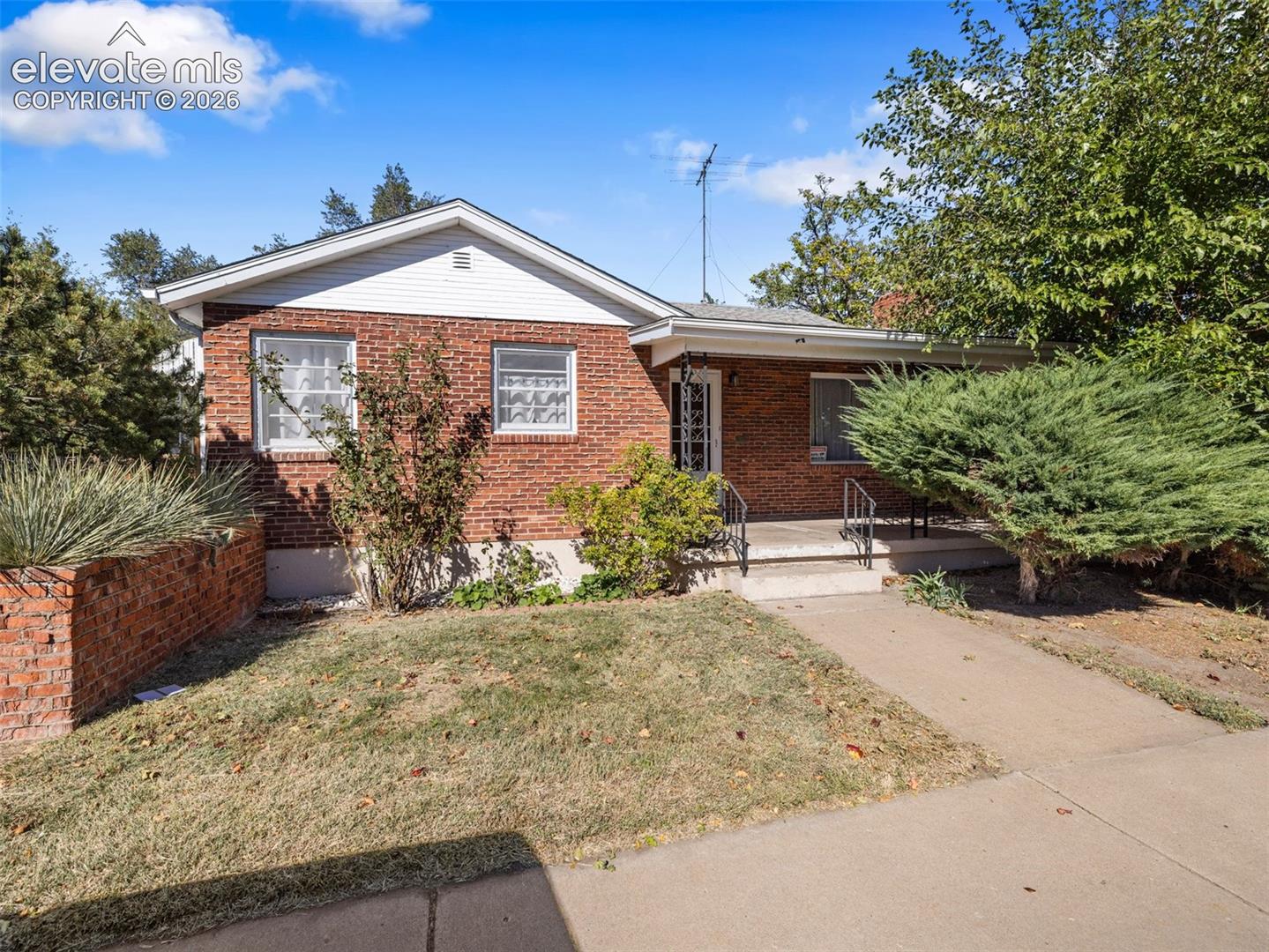Single-story brick exterior featuring a covered front porch, white lap siding gables, and a masonry retaining wall
