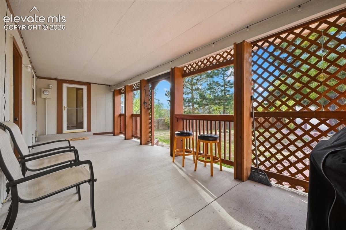 Covered patio featuring an exterior entry door, concrete flooring, and lattice detailing