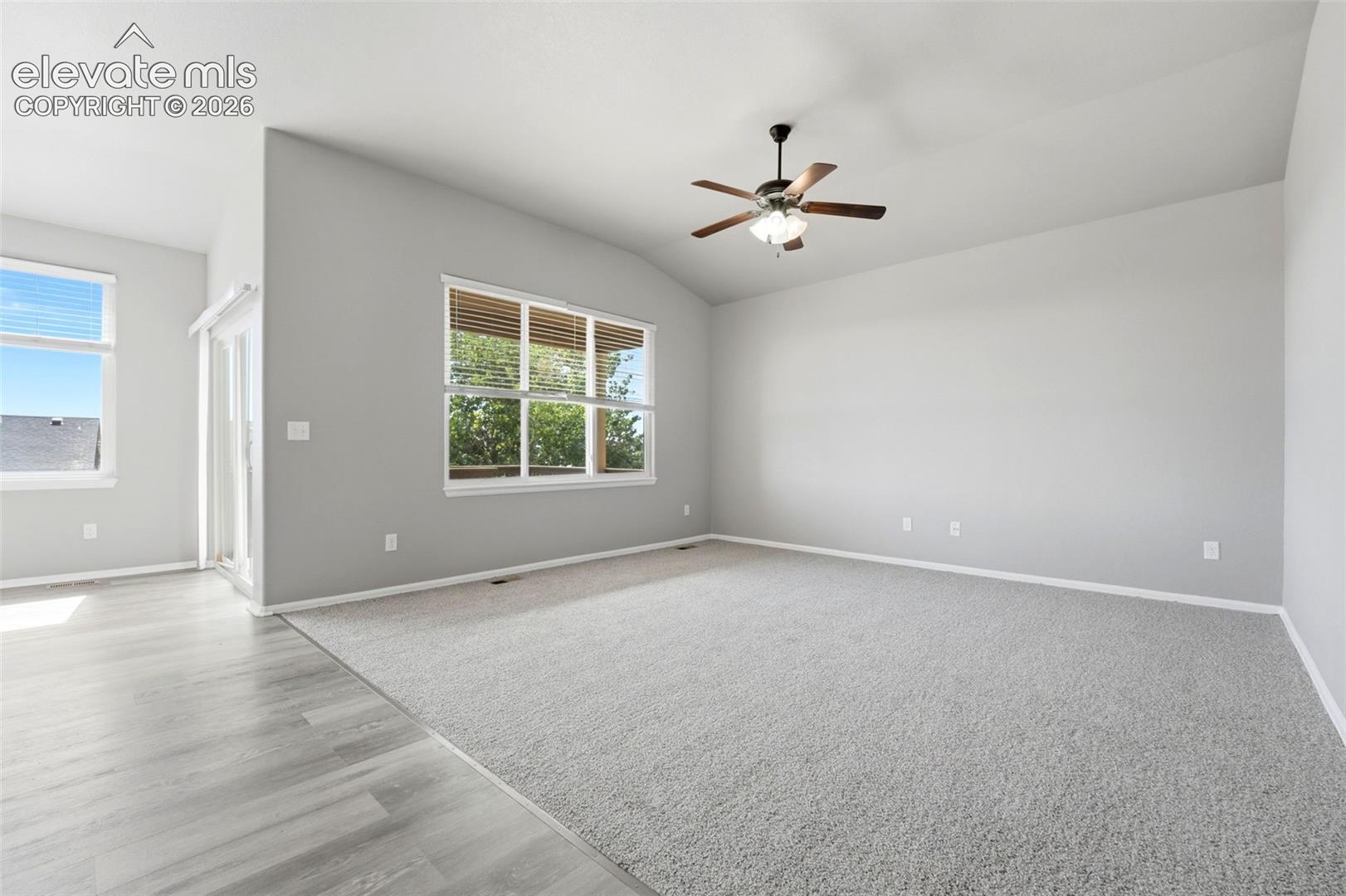 Vaulted ceiling with a ceiling fan, light gray carpeting, wood-finish flooring, and multiple windows