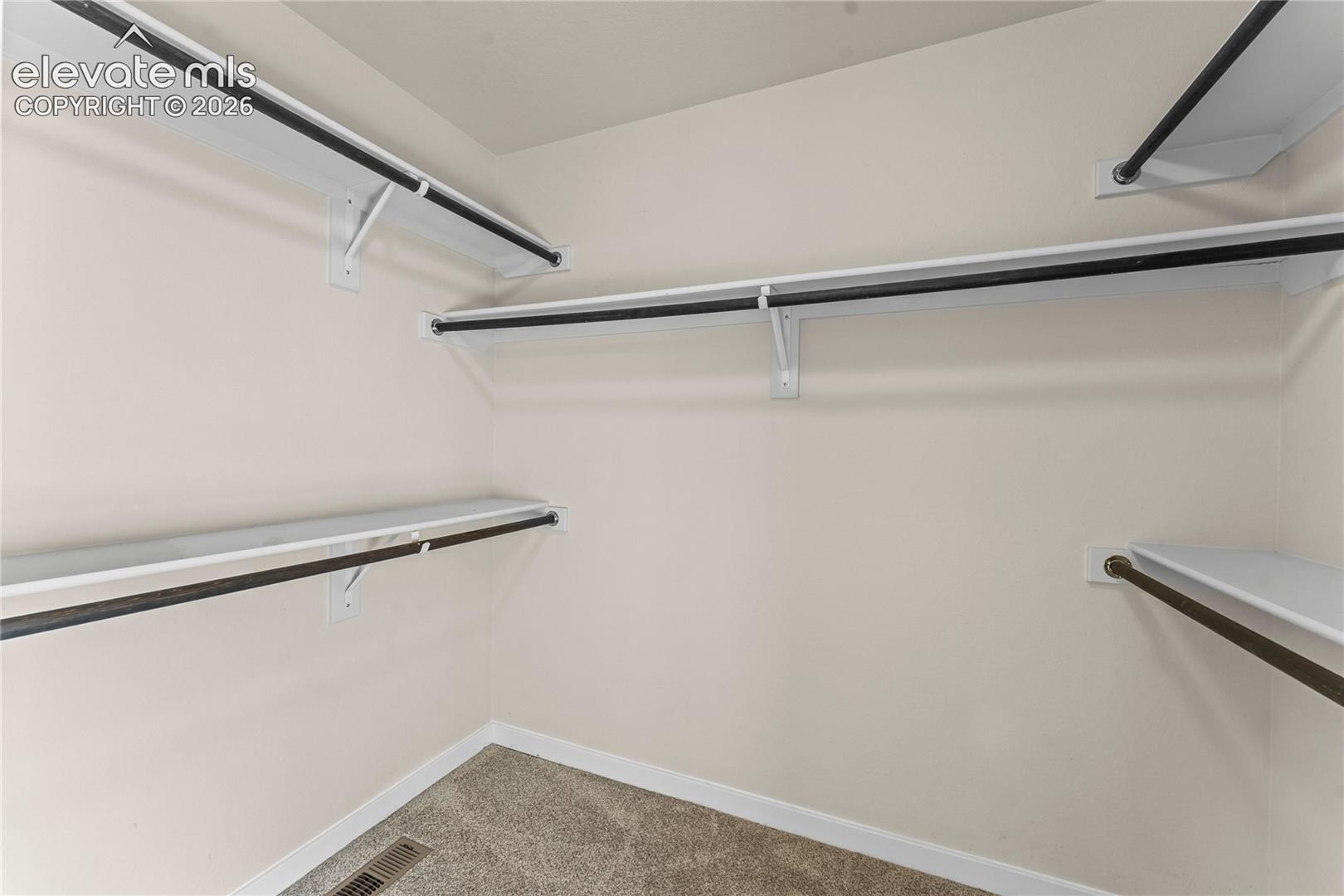 Storage area featuring multi-level white shelving and integrated metal hanging rods
