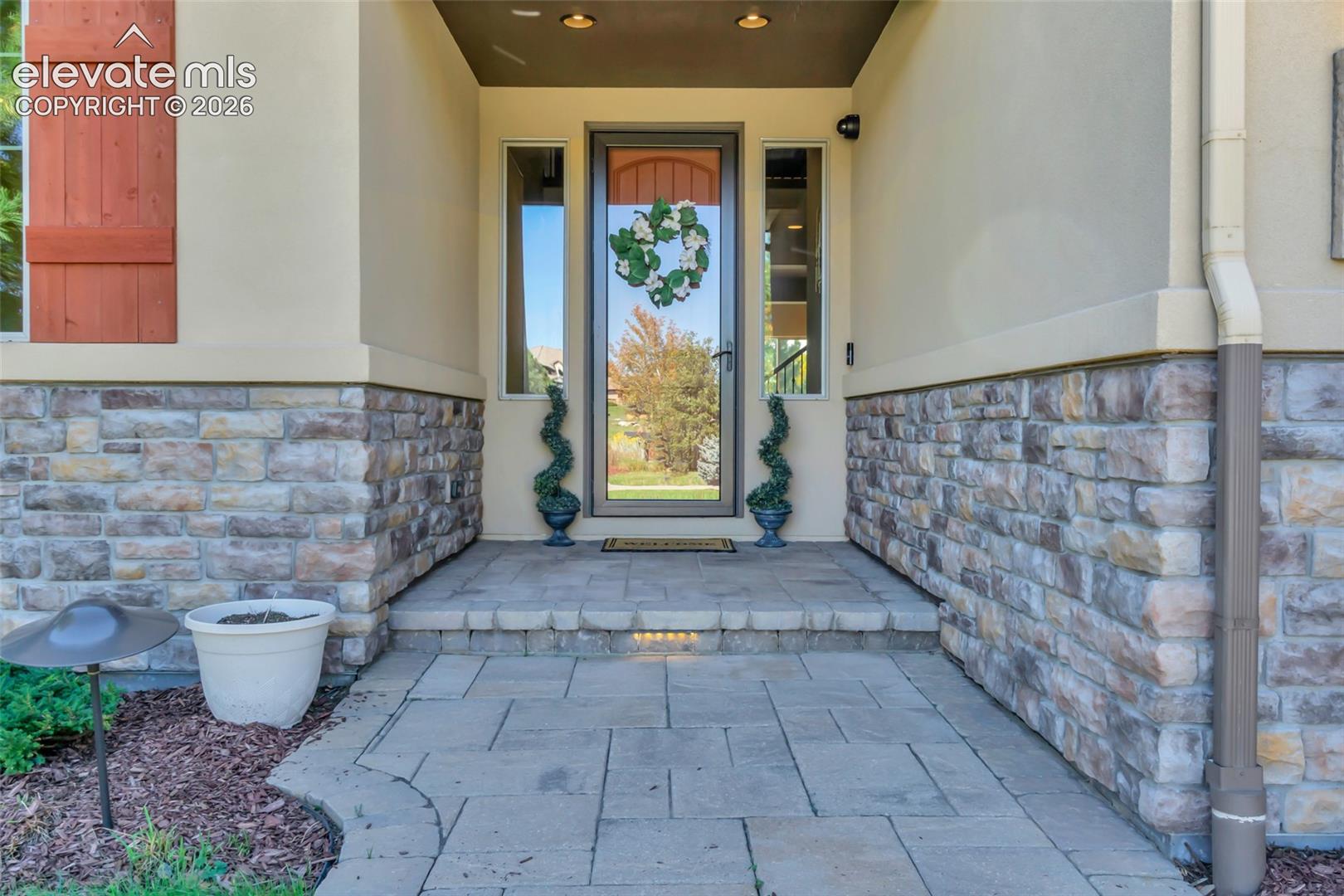 Covered entryway featuring a stone veneer facade, paved walkway, glass-paneled front door, and flanking side lights