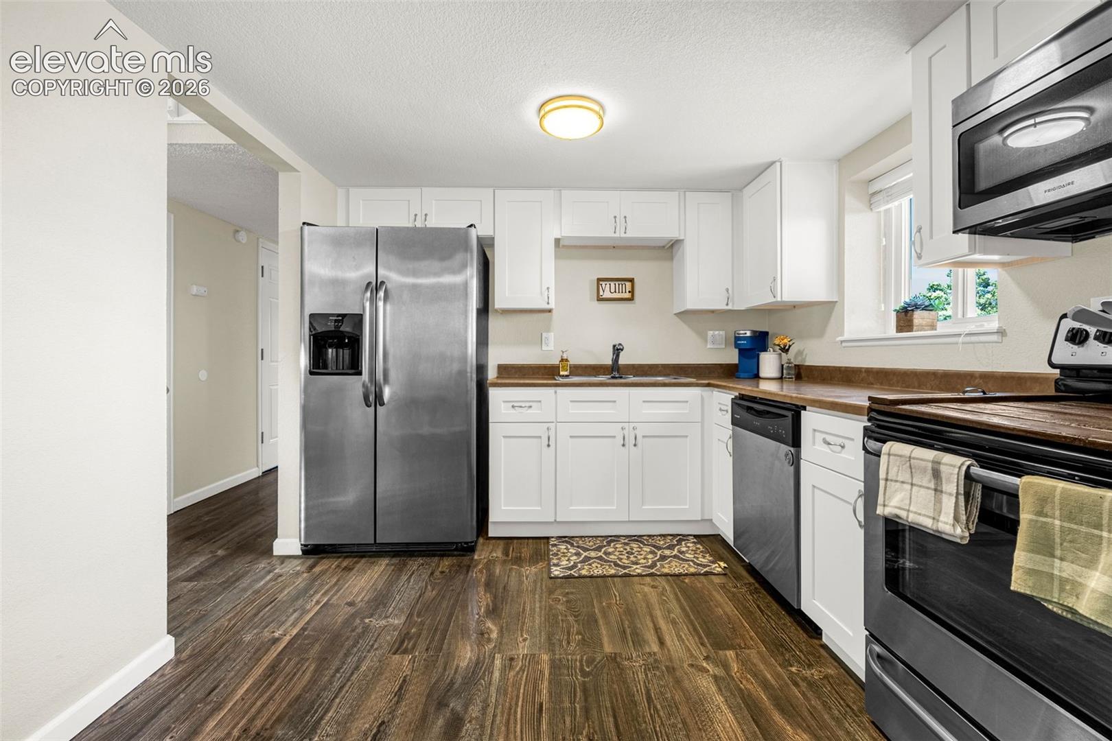 Kitchen featuring white shaker-style cabinetry, wood-finish flooring, stainless steel appliances, and a flush-mount ceiling light