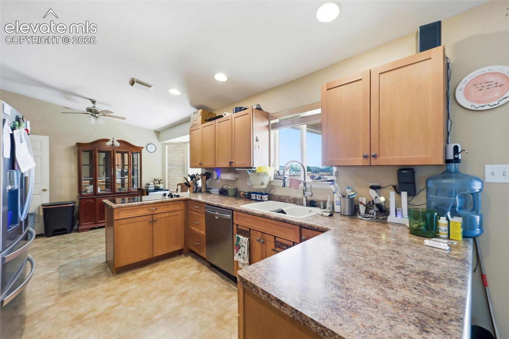Spacious kitchen featuring light wood cabinetry, a double basin sink, stainless steel dishwasher, and textured countertops