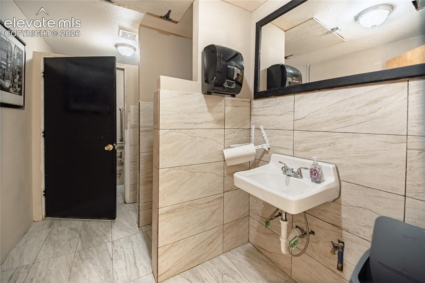 White wall-mounted sink with chrome fixtures, set against light-toned tiled walls