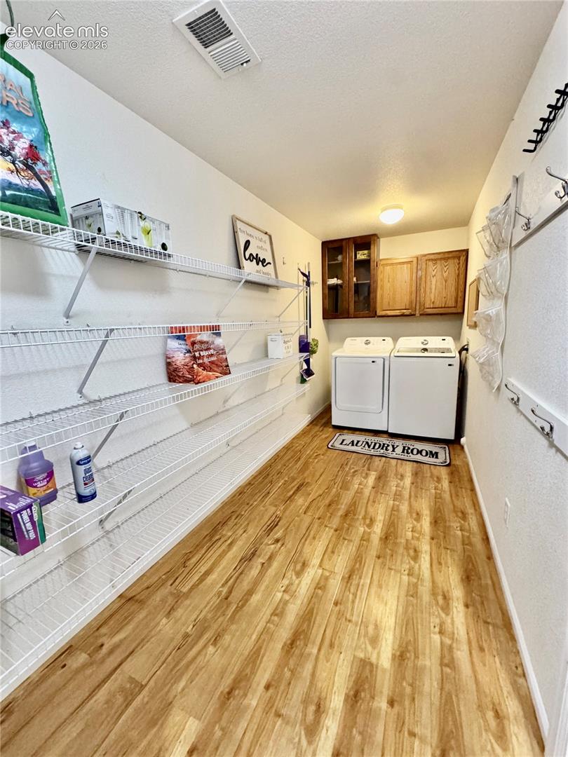Dedicated laundry area with wood-finish flooring, overhead lighting, and built-in wall shelving