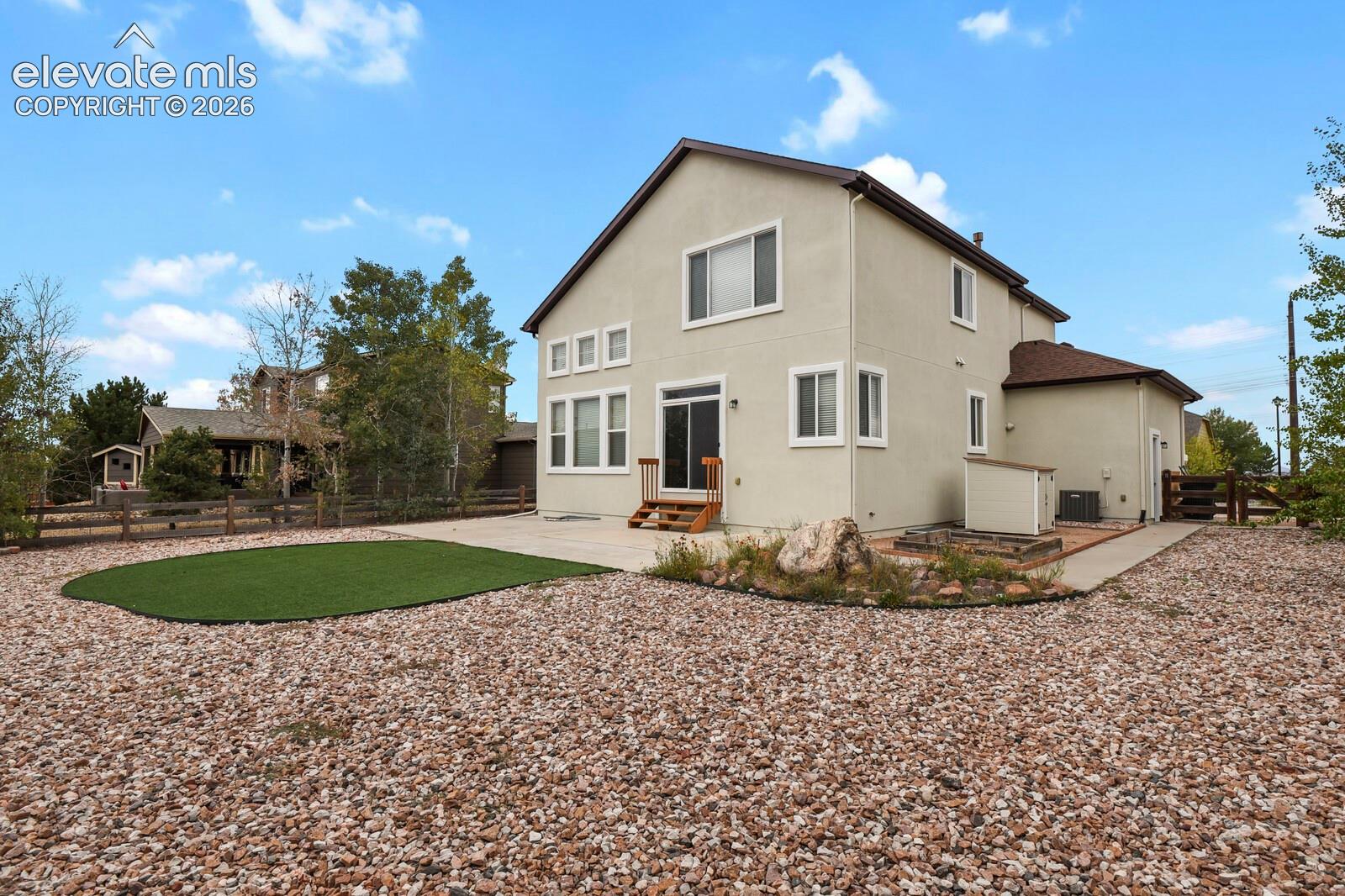 Exterior with stucco finish, multiple windows, sliding glass door, patio area, and a low-maintenance gravel yard with an artificial turf section