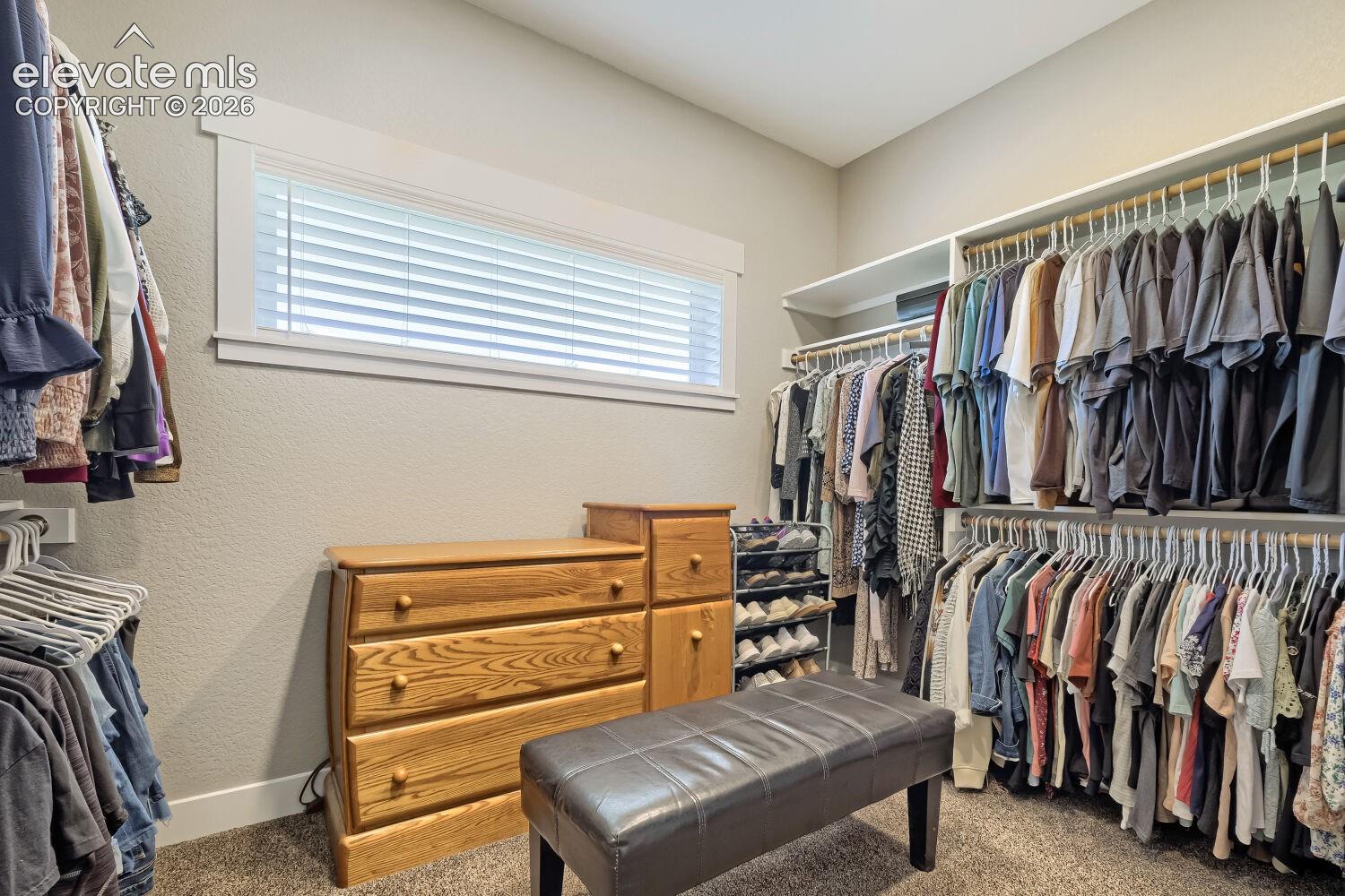 Built-in closet organization system with multiple hanging rods and shelving, textured wall finish, and a horizontal window with blinds