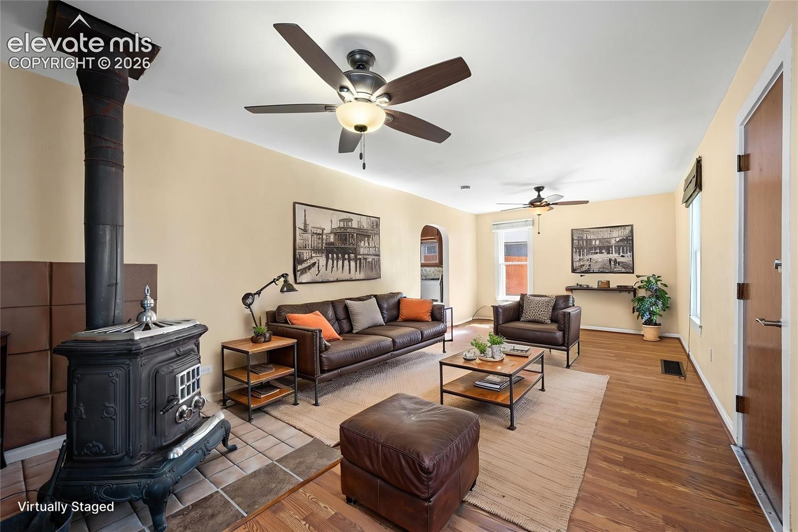 Living area featuring a cast-iron wood-burning stove, tile hearth, wood-finish flooring, and dual ceiling fans
