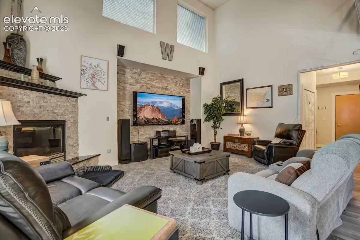 Living room featuring a stacked stone fireplace with a dark mantel, a complementary stacked stone accent wall, high ceilings, transom windows, and dark wood-finish flooring