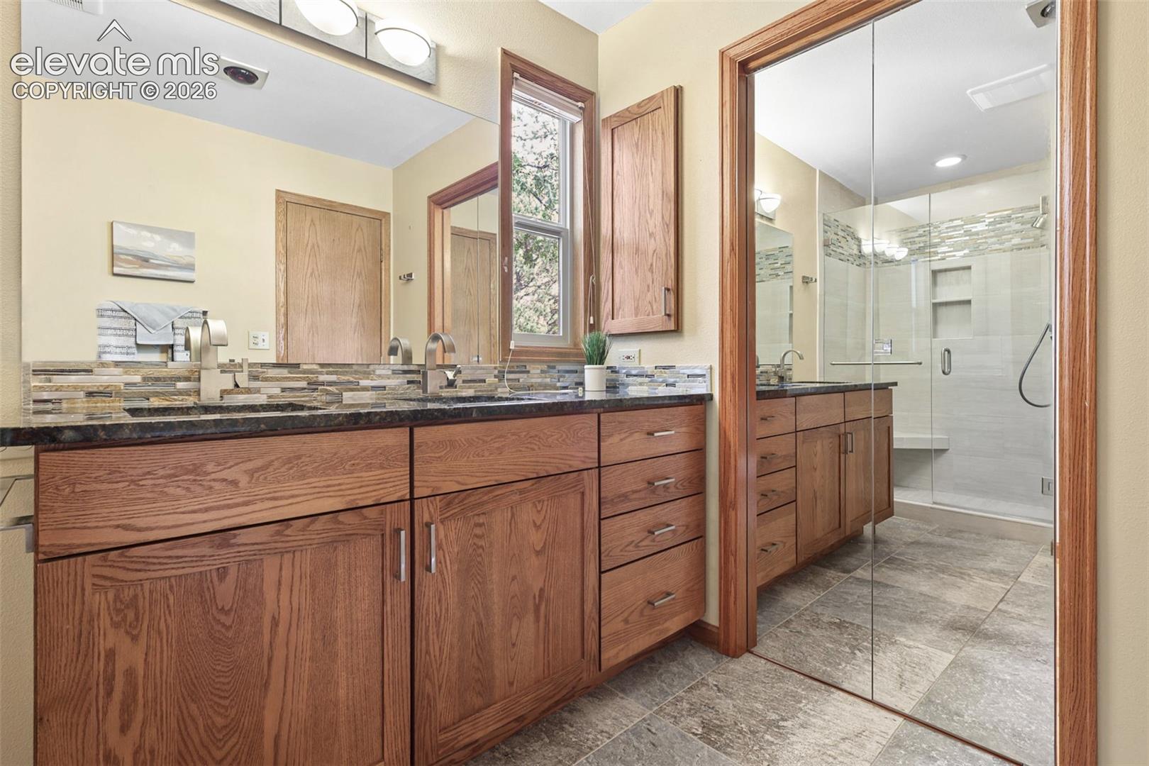Primary remodeled bath features double sinks, granite counters, and stone flooring.  The walk-in closet is behind the mirrored doors.