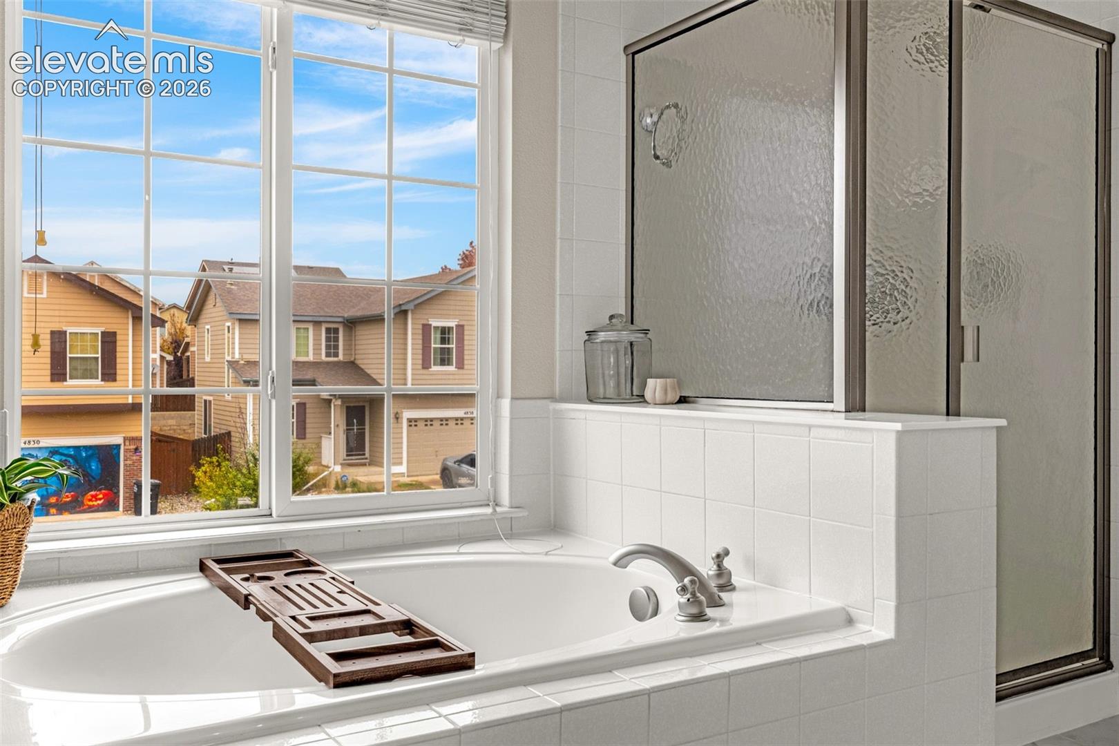 Oversized soaking tub featuring a tiled surround, integrated shower with a glass enclosure, and a large multi-pane window
