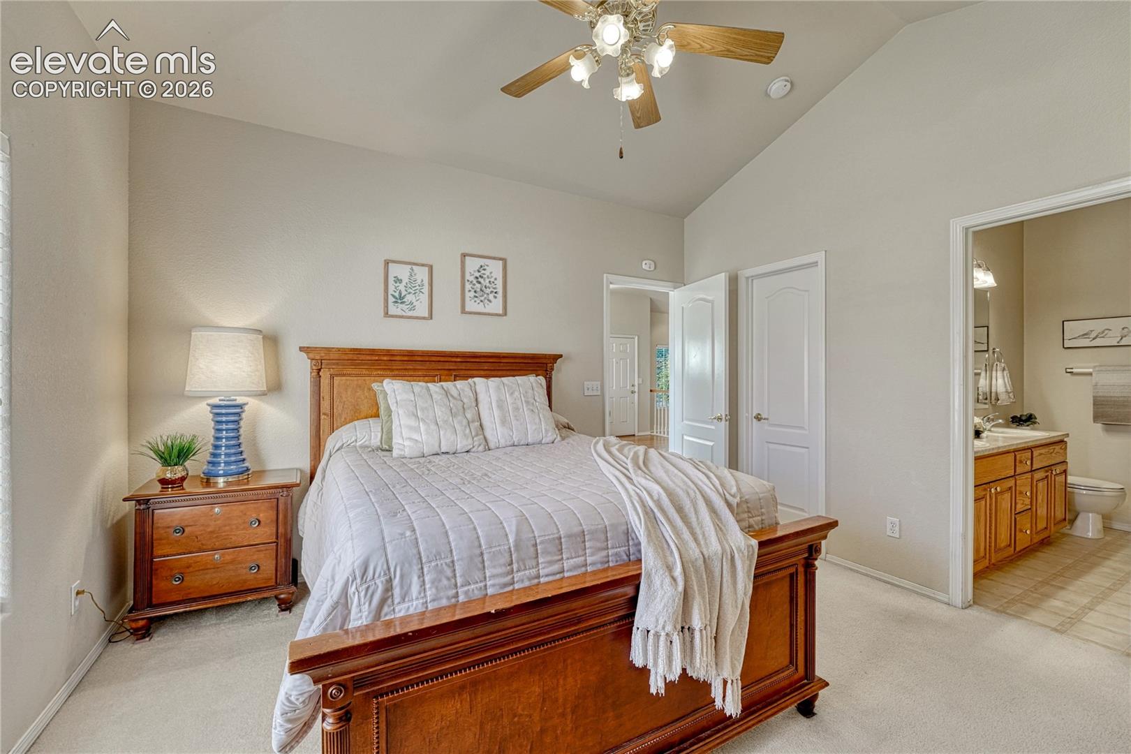 The primary suite serves as a serene main-level retreat featuring vaulted ceilings, a ceiling fan, plush carpet, and an adjoining private bath
