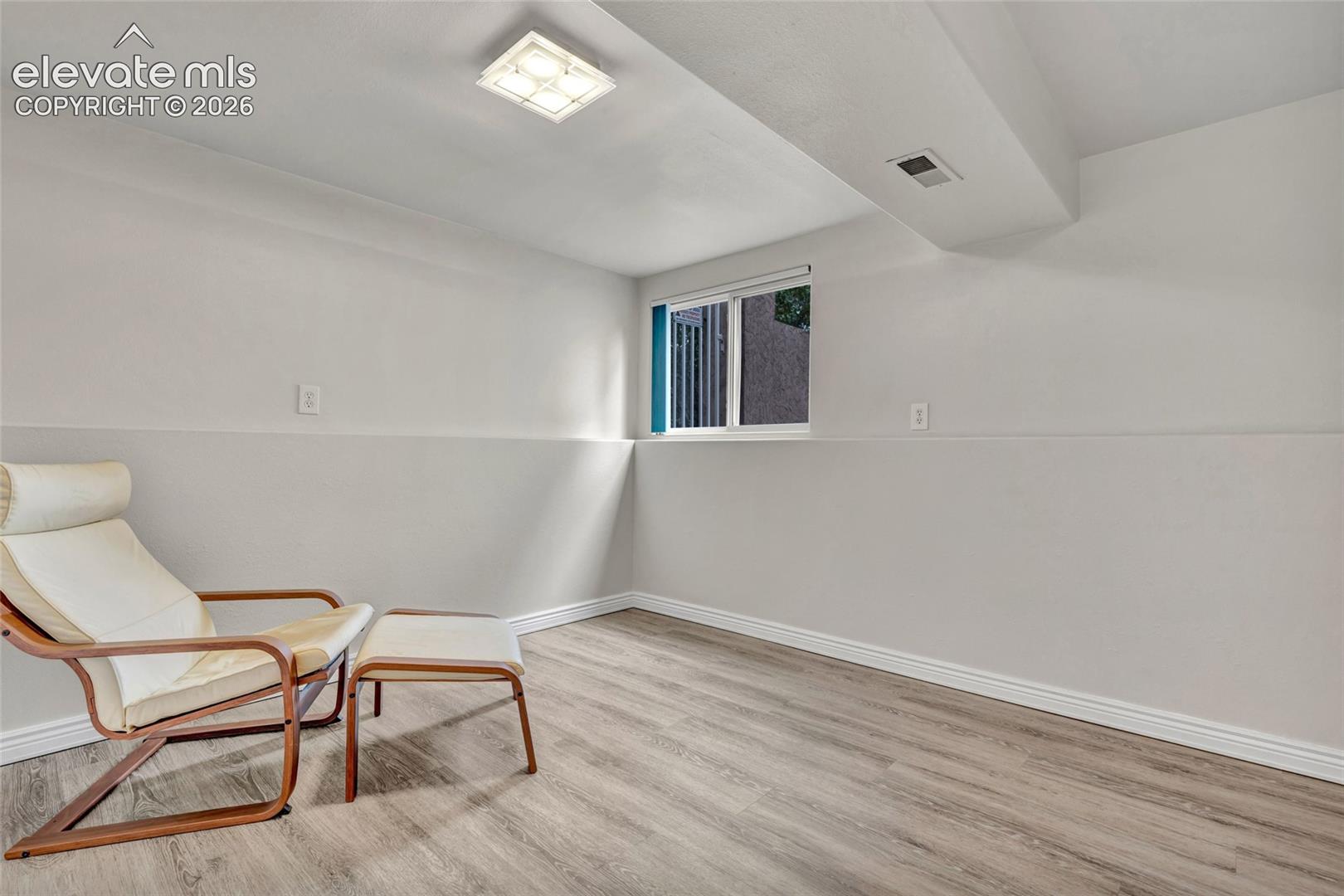 Versatile lower-level room featuring light wood-finish flooring, neutral painted walls, and a recessed window