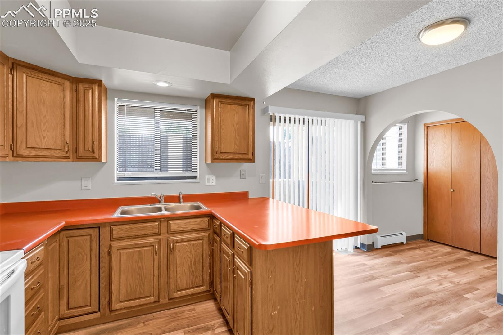 Kitchen with a peninsula, healthy amount of natural light, light wood finished floors, arched walkways, and a textured ceiling