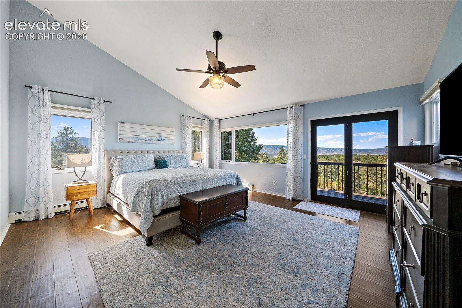 Vaulted ceilings, wood-finish flooring, ceiling fan with integrated lighting, expansive windows, and glass-paneled exterior doors