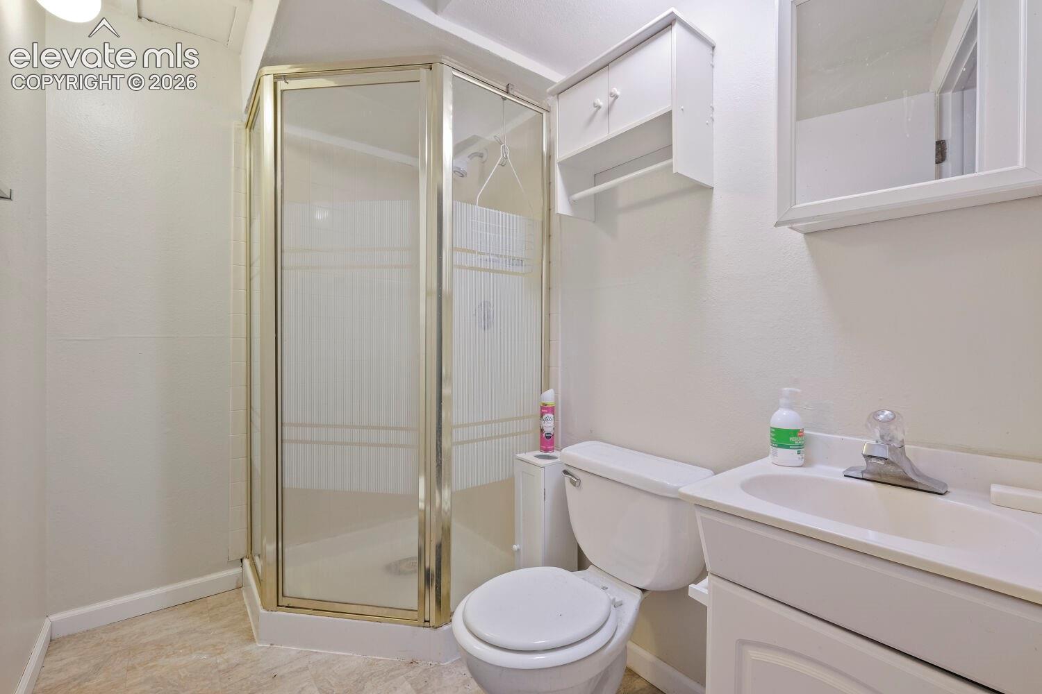 Bathroom featuring a corner shower enclosure, white vanity with integrated sink, wall-mounted medicine cabinet, white toilet, and neutral-toned flooring