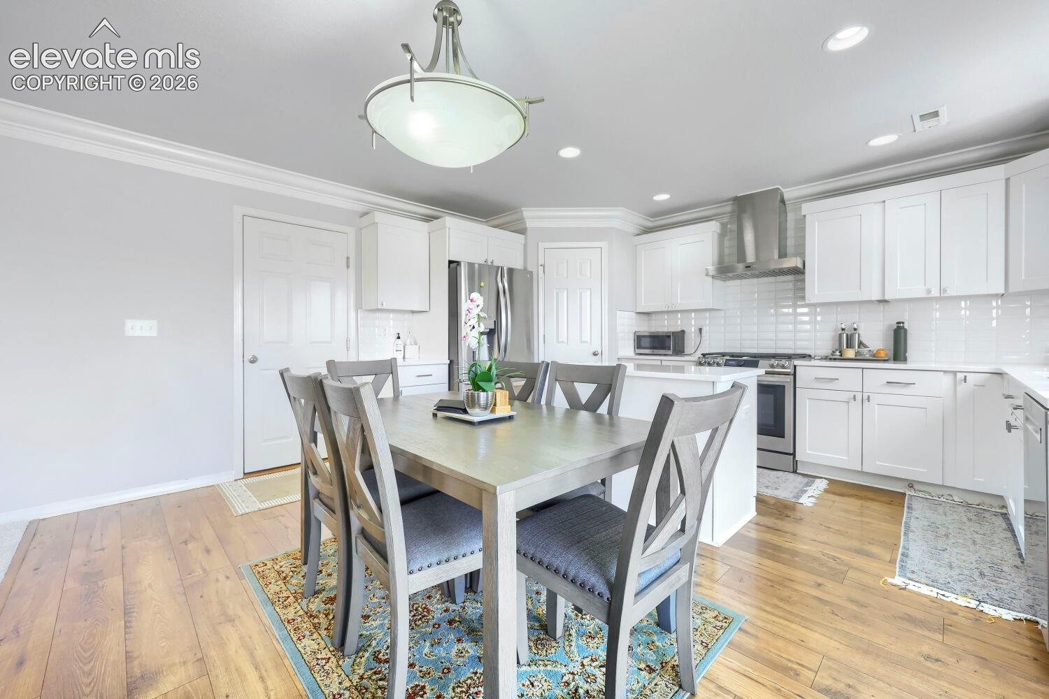 Kitchen featuring white shaker-style cabinetry, stainless steel appliances, subway tile backsplash, crown molding, and wood-finish flooring