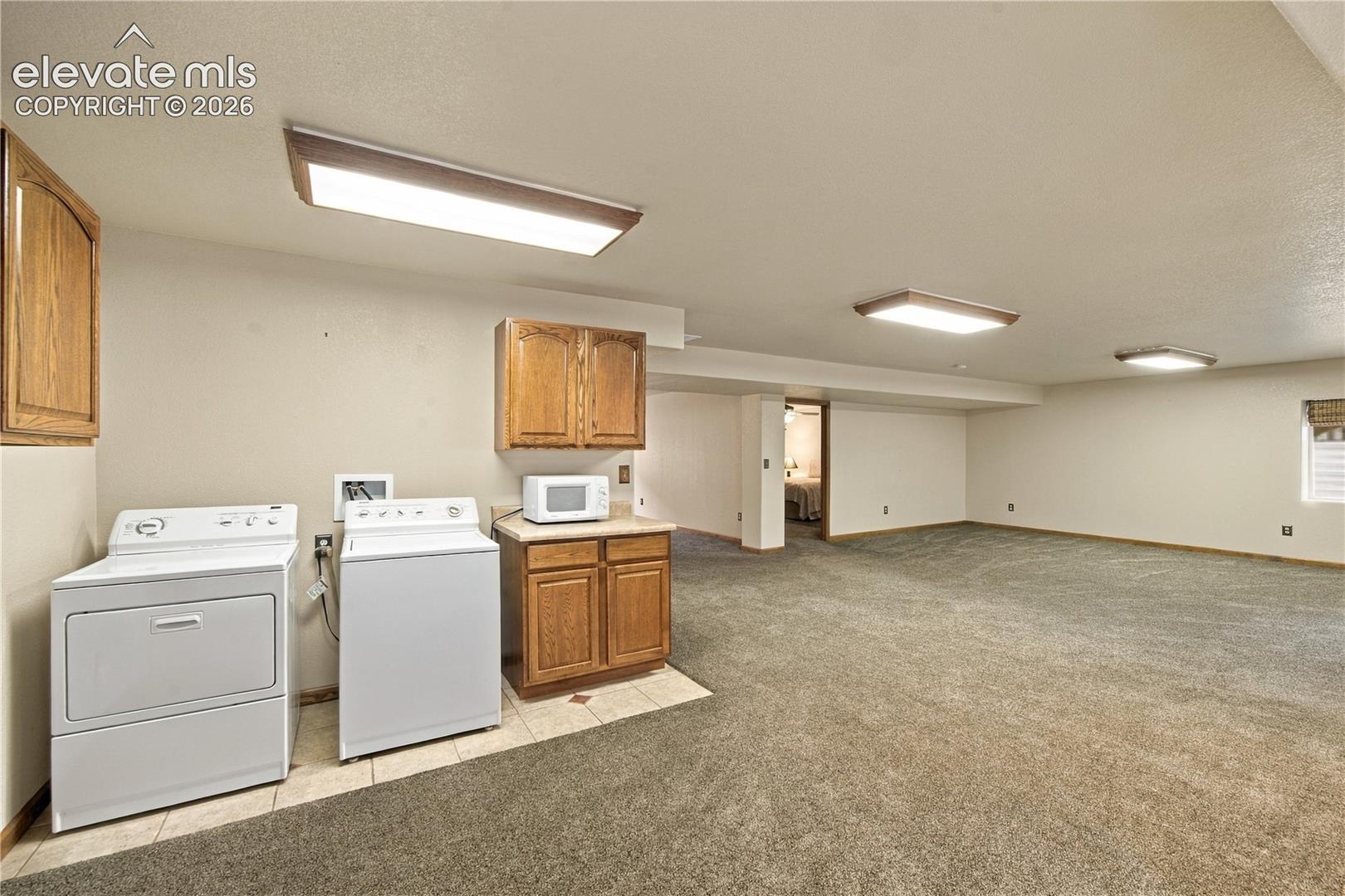 Open-concept space featuring wall-to-wall carpeting, recessed lighting fixtures, built-in wooden cabinetry, and dedicated laundry hookups with tile flooring