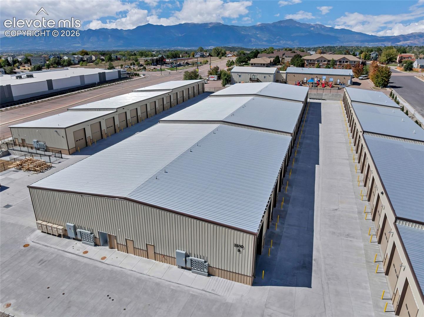 Mountain backdrop, multiple storage buildings, light-colored metal roofing, beige and brown siding, paved lot