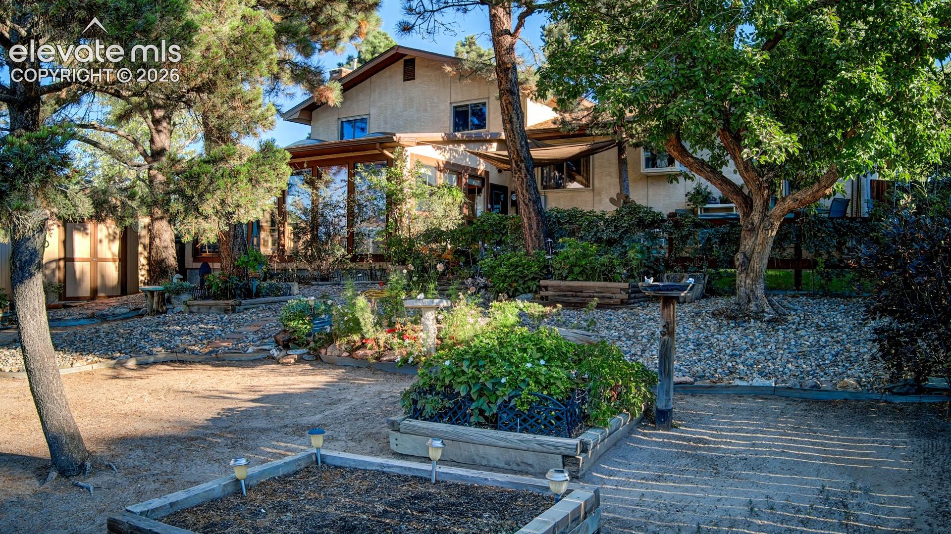 Expansive exterior featuring mature trees, a sunroom with large windows, and multiple raised garden beds