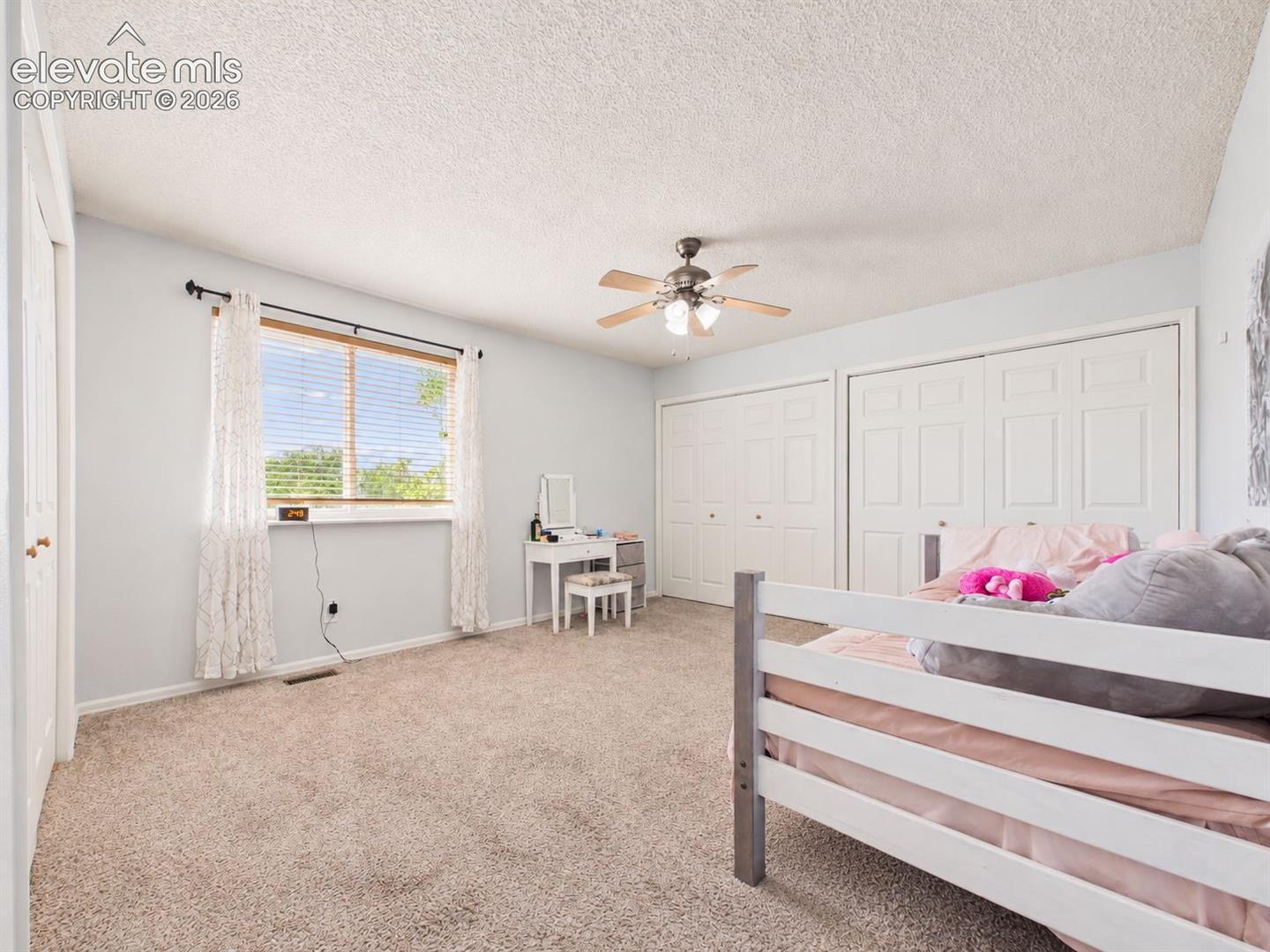 Bright secondary bedroom features a large window, ceiling fan, neutral finishes, and substantial closet space along the wall.