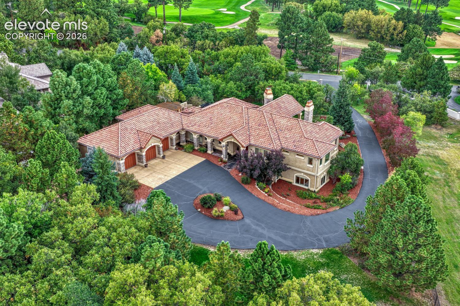 Single-level residence with a multi-gabled tile roof, masonry chimneys, and a circular asphalt driveway