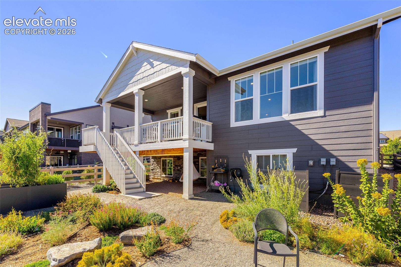 Exterior featuring dark gray horizontal siding, a covered upper-level deck with white railing, and a lower-level gravel landscaping area with various plantings