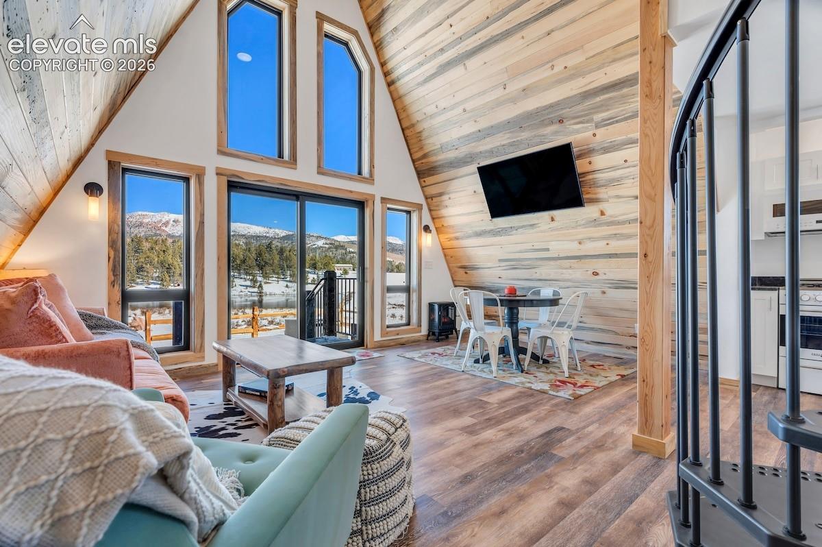 A-frame architecture featuring natural wood plank wall treatments, expansive multi-pane windows, wood-finish flooring, and a metal spiral staircase