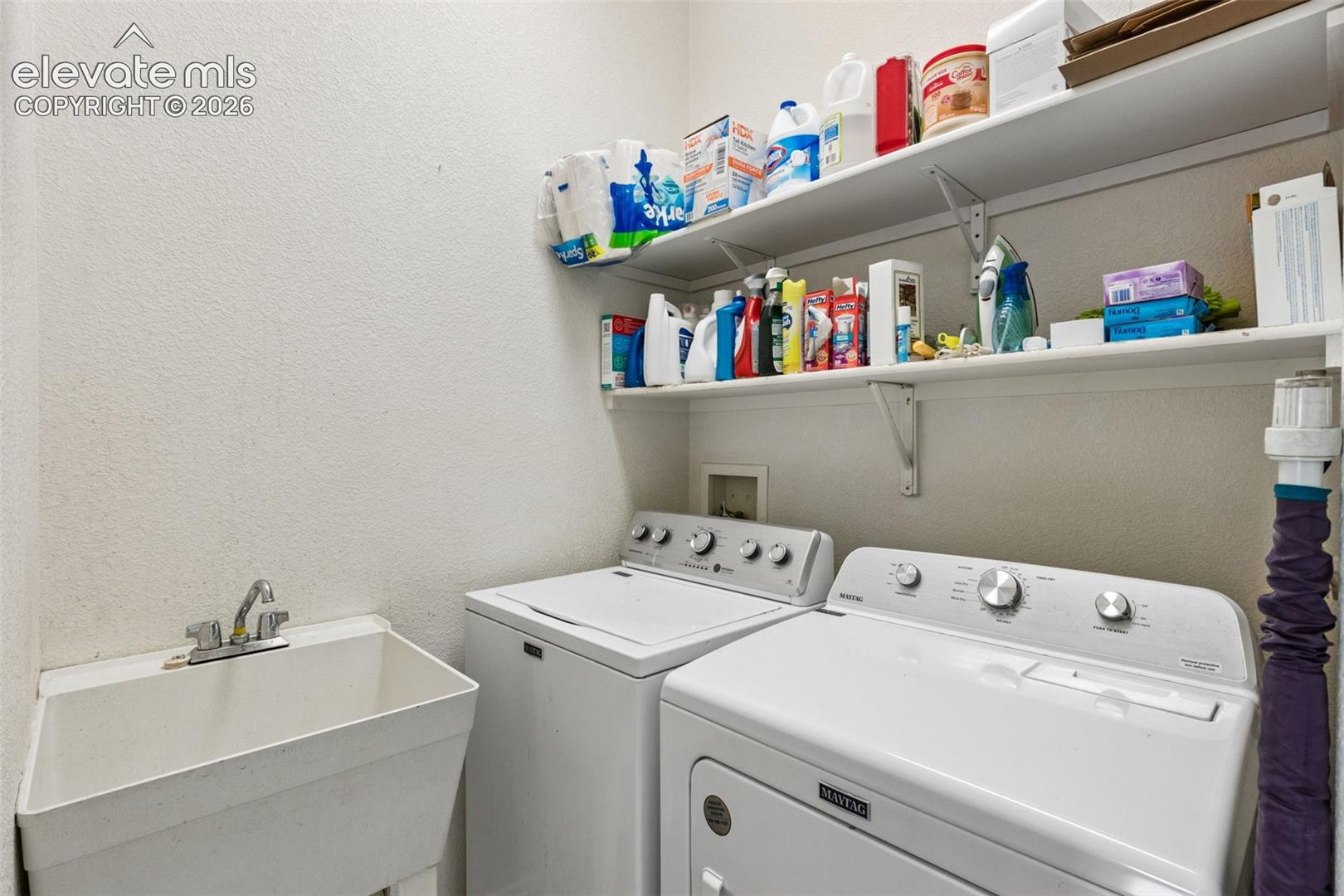 Utility area featuring a deep-basin drop-in sink with a chrome faucet, dual wall-mounted storage shelves, and dedicated connections for laundry appliances