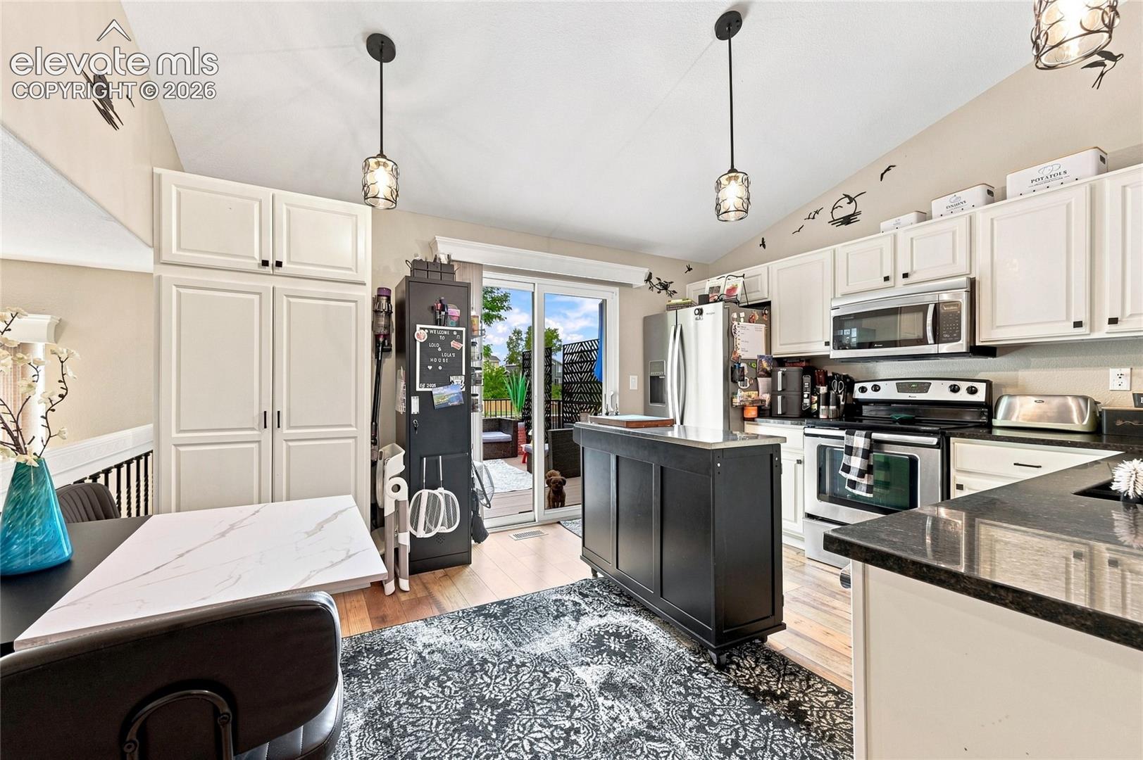 Kitchen featuring white cabinetry, dark countertops, vaulted ceilings with pendant lighting, and sliding glass doors