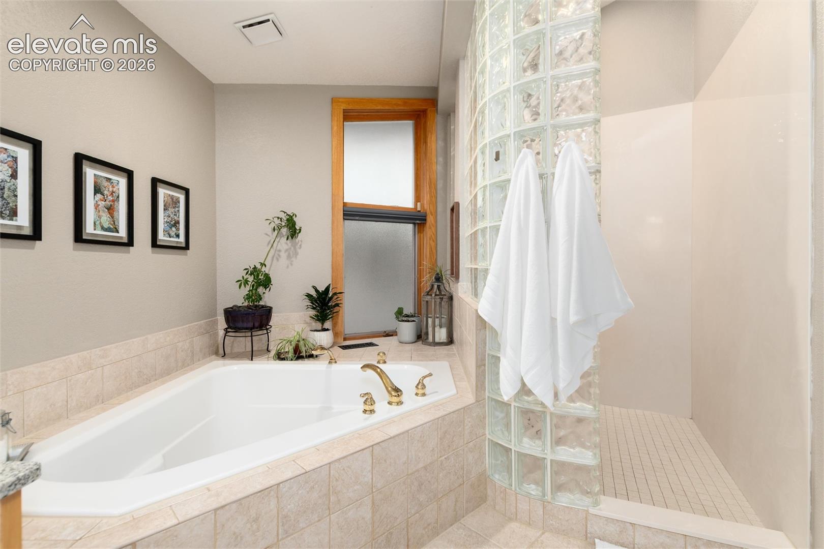 Soaking tub with brass fixtures, surrounded by neutral-toned tiled decking