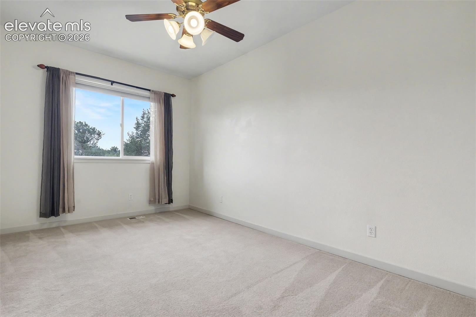 Spacious room featuring neutral carpeting, a large window, and a ceiling fan with integrated lighting