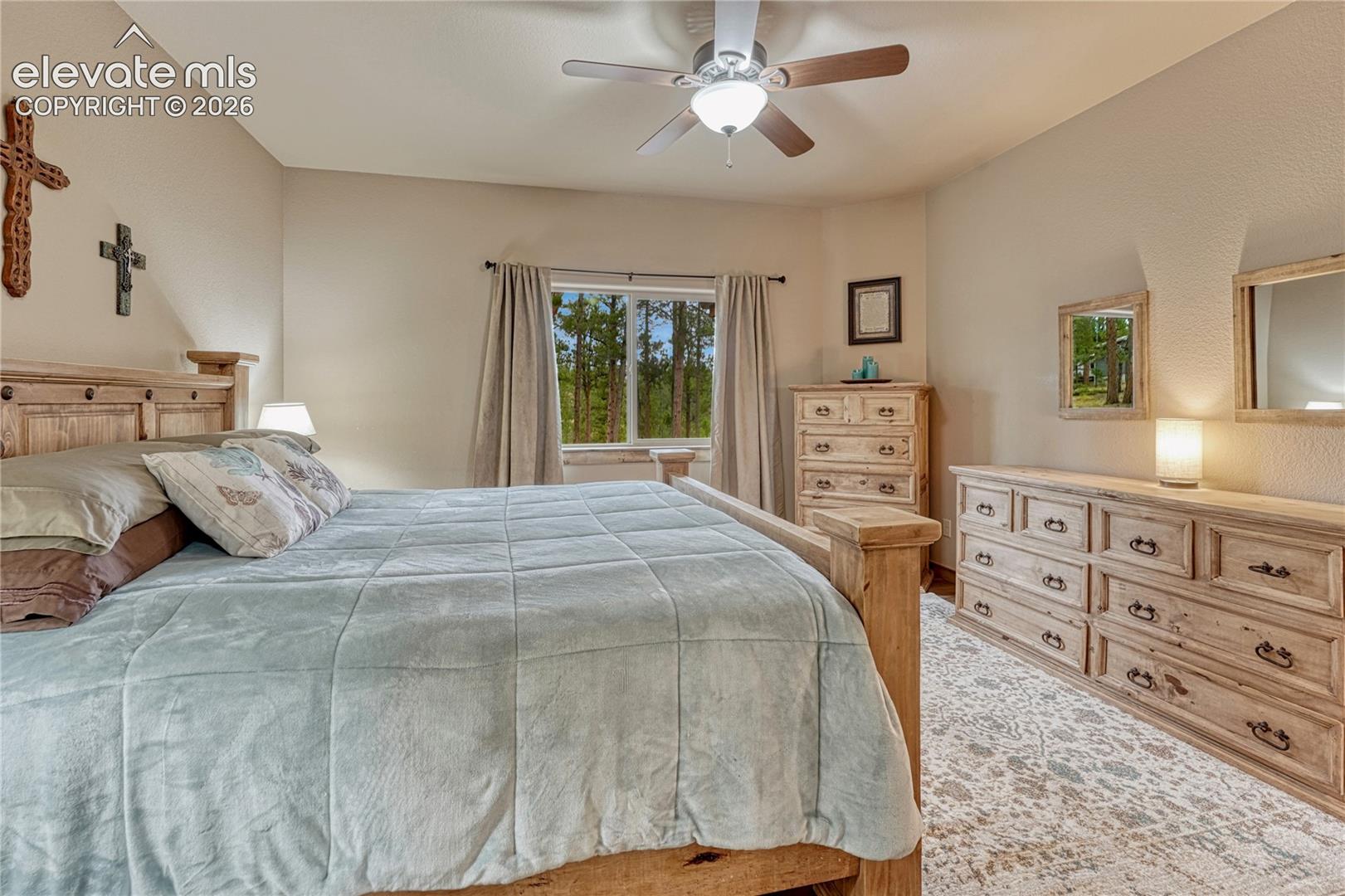 Bedroom featuring a ceiling fan with integrated lighting and a window with exterior forest scenery