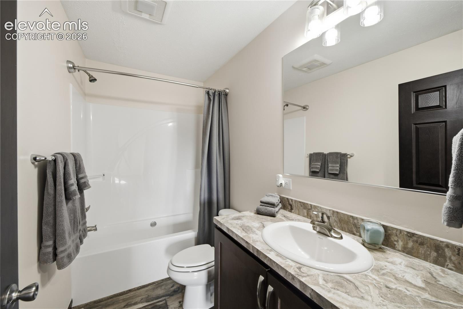 Bathtub with shower, single vanity with integrated sink, dark wood-finish cabinetry, and a large wall-mounted mirror