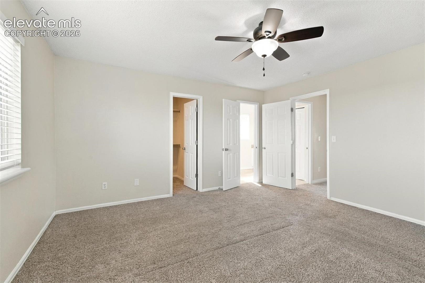 Neutral-toned interior room featuring wall-to-wall carpeting, a ceiling fan with integrated lighting, and multiple interior doors with six-panel detailing