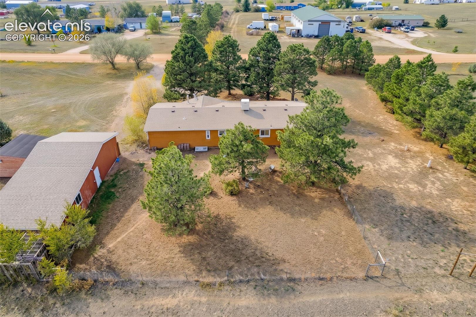 Aerial perspective of a single-story residence featuring a detached garage, mature evergreen trees, and expansive acreage