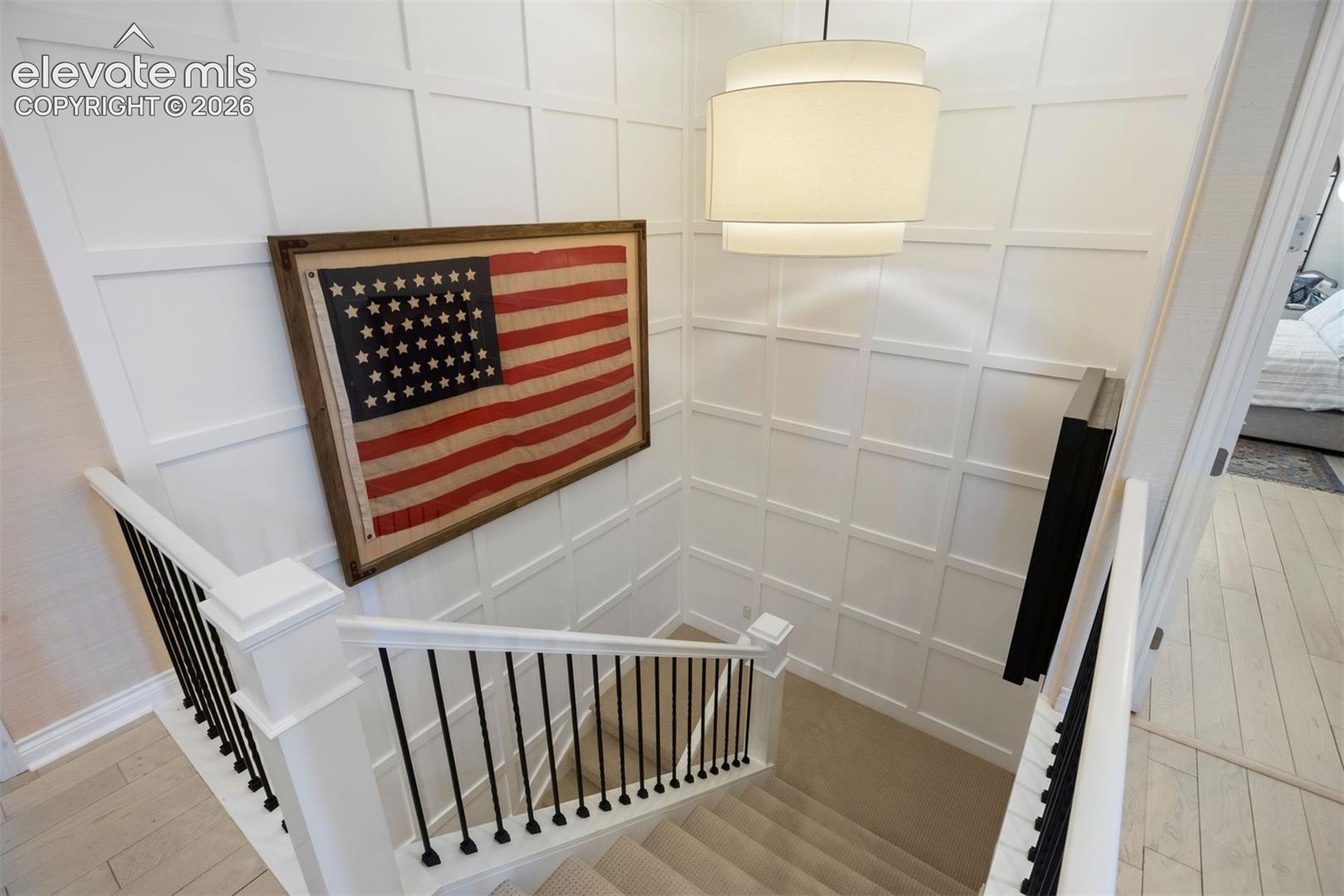 Stairwell featuring white wainscoting, a contemporary drum pendant light, and a carpeted staircase with white newel posts and black metal balusters