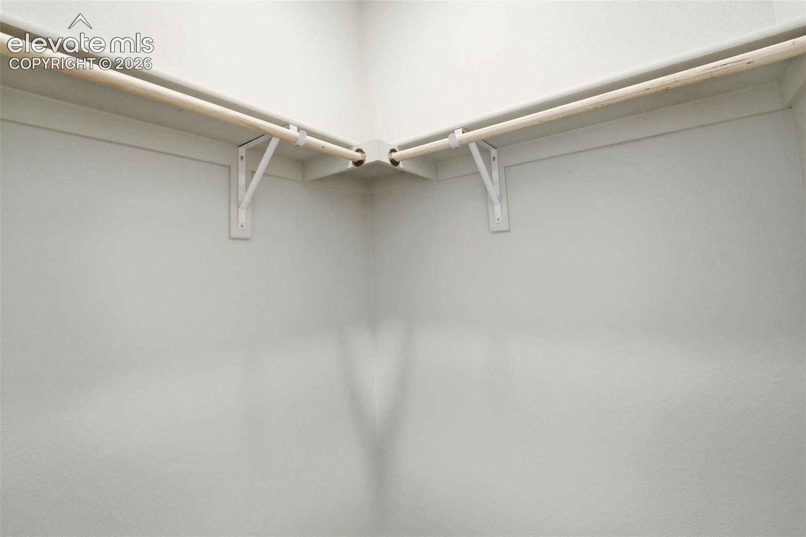 Walk-in closet featuring dual-level wooden hanging rods and integrated corner shelving supported by white metal brackets