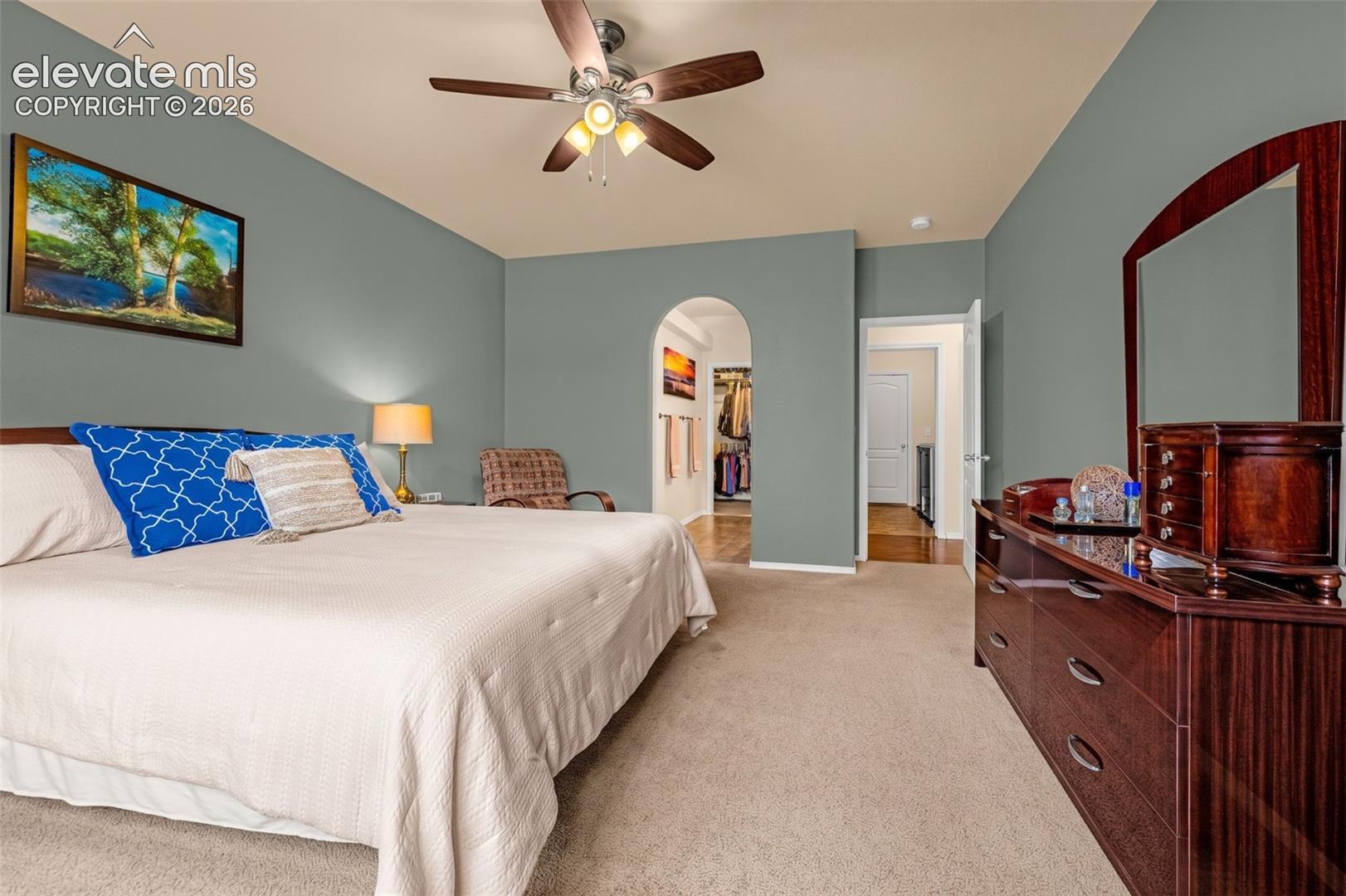 Room featuring neutral-toned carpeting, a central ceiling fan with integrated light fixture, and an arched entryway