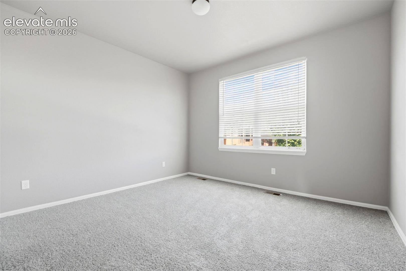 Neutral-toned walls with light grey carpeting, white window blinds, and overhead lighting