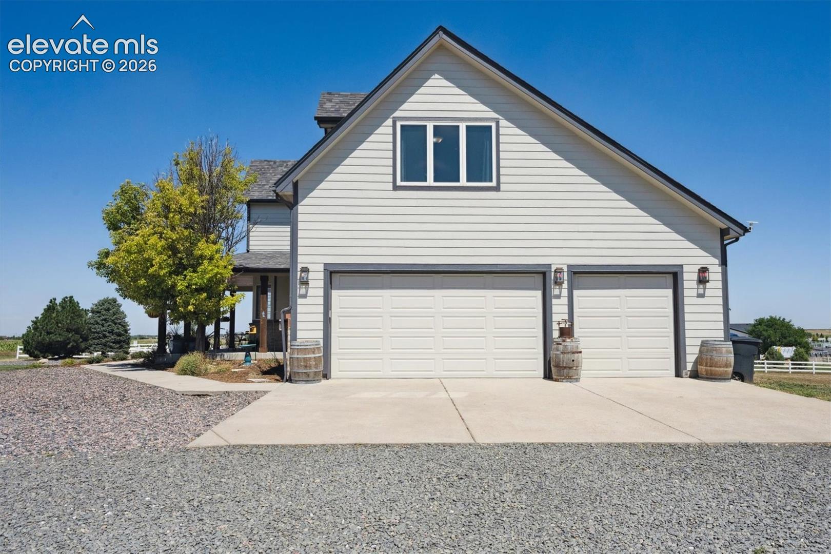 Impressive side profile showcasing an expansive attached 3 car garage setup featuring a double-bay door alongside a single-bay door, generous concrete apron parking, and a large gravel driveway. Accented by exterior coach lights, and clean horizontal siding with contrasting dark trim, this entry offers ample room for vehicles, storage, or recreational gear.