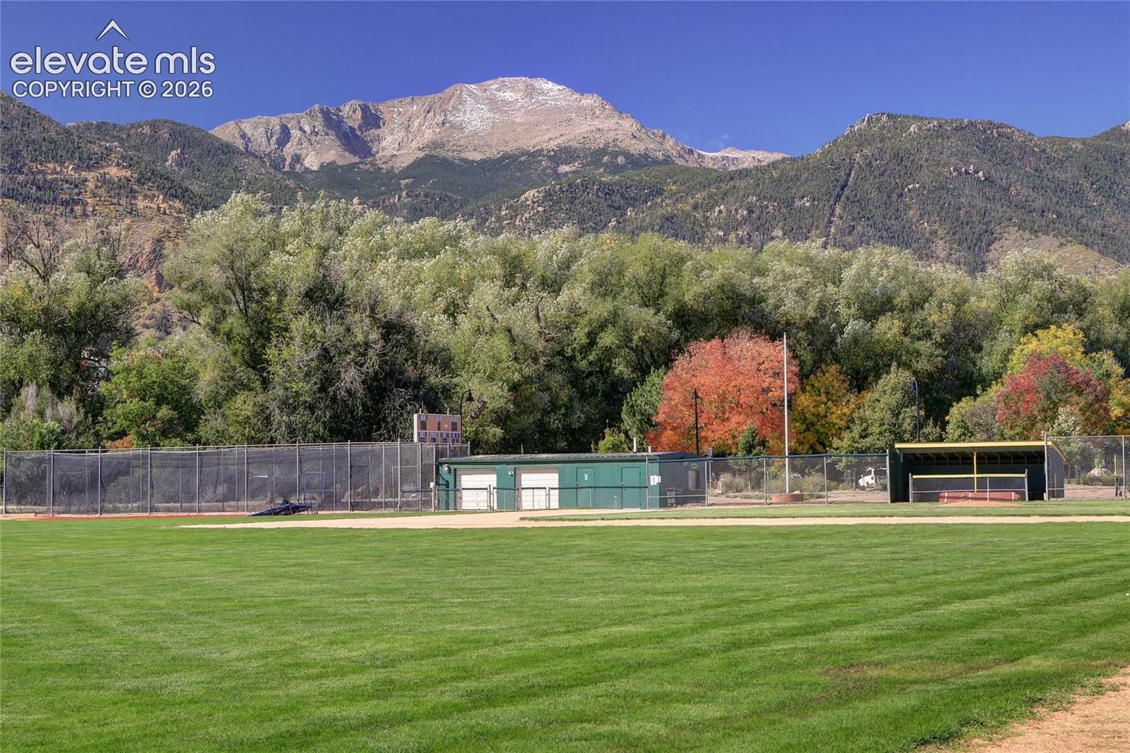 Expansive grounds featuring a manicured grass field, ball diamond, chain-link fencing, and a mountain backdrop