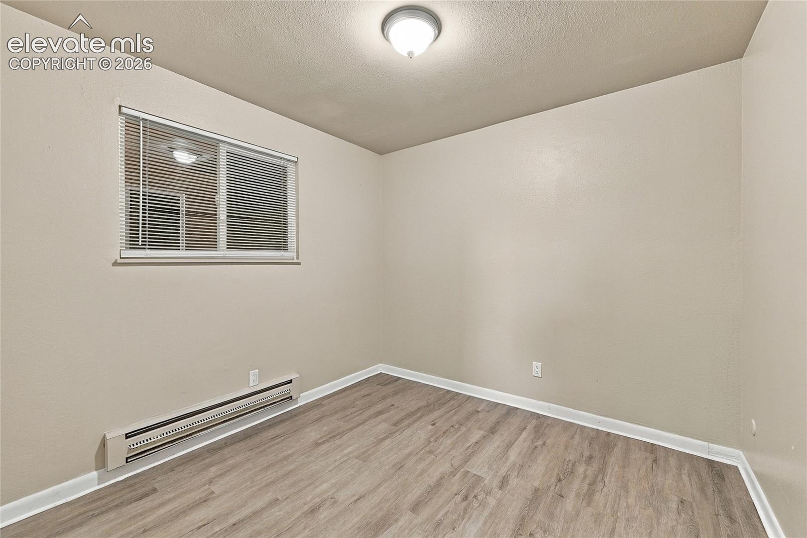 Room featuring wood-finish flooring, neutral wall paint, a sliding window with horizontal blinds, and a central dome-style ceiling light fixture