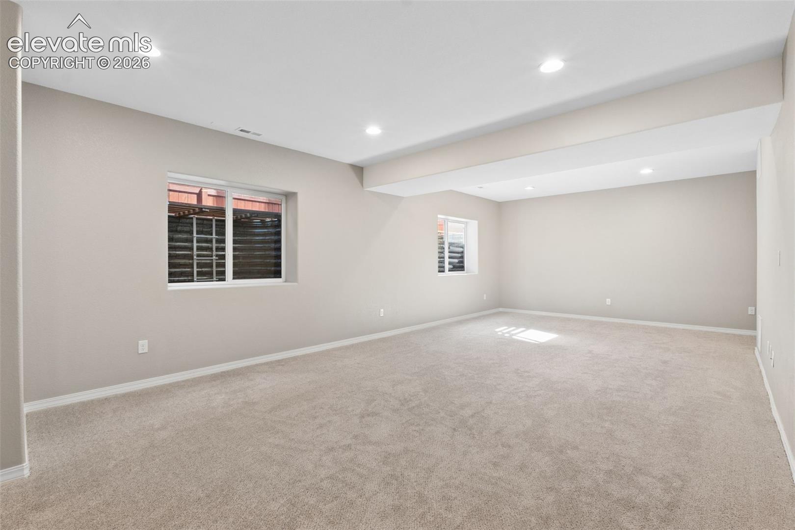 Spacious room featuring neutral carpeting, recessed lighting, two windows, and light-toned walls with white trim