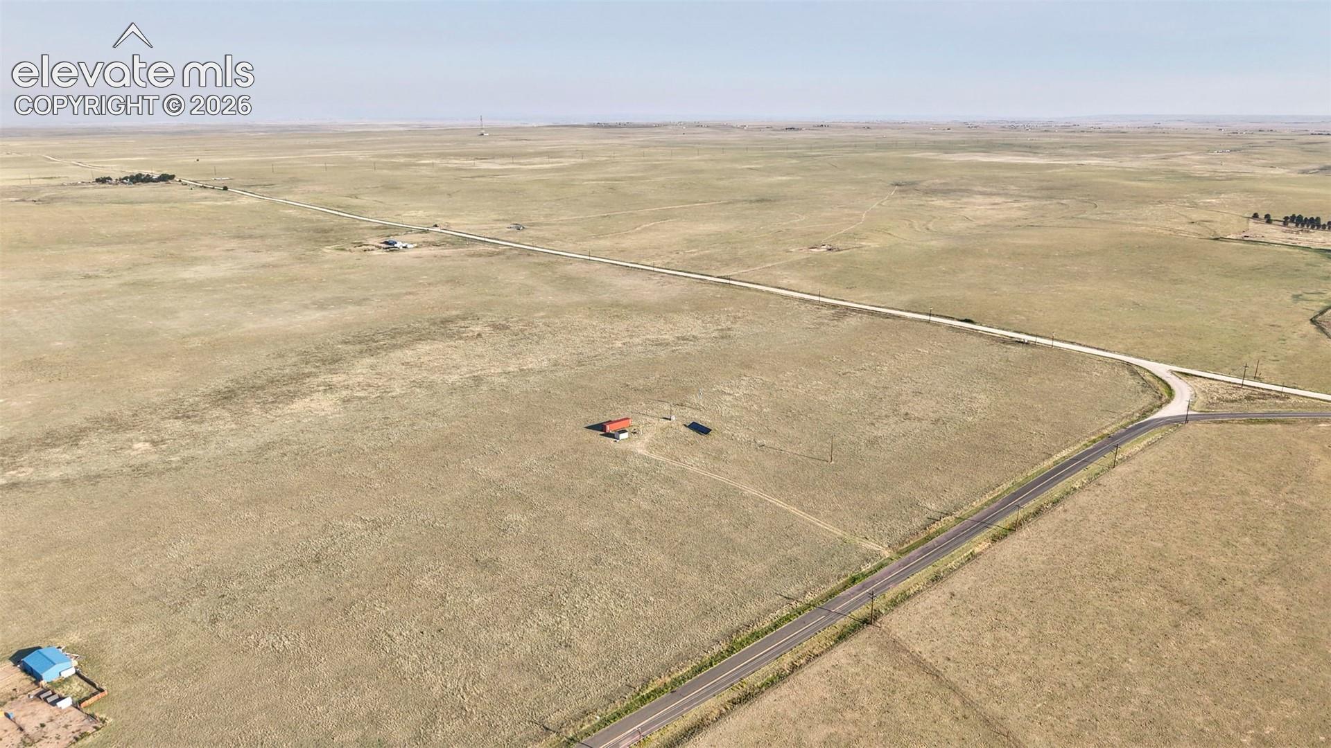 Expansive undeveloped land with a partial paved road frontage and a dirt road intersection
