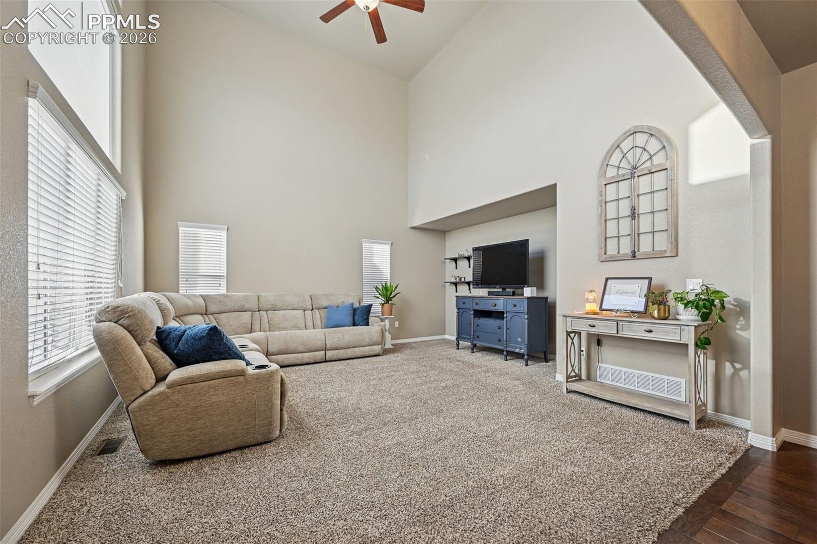 Living room featuring ceiling fan, a high ceiling, and dark carpet